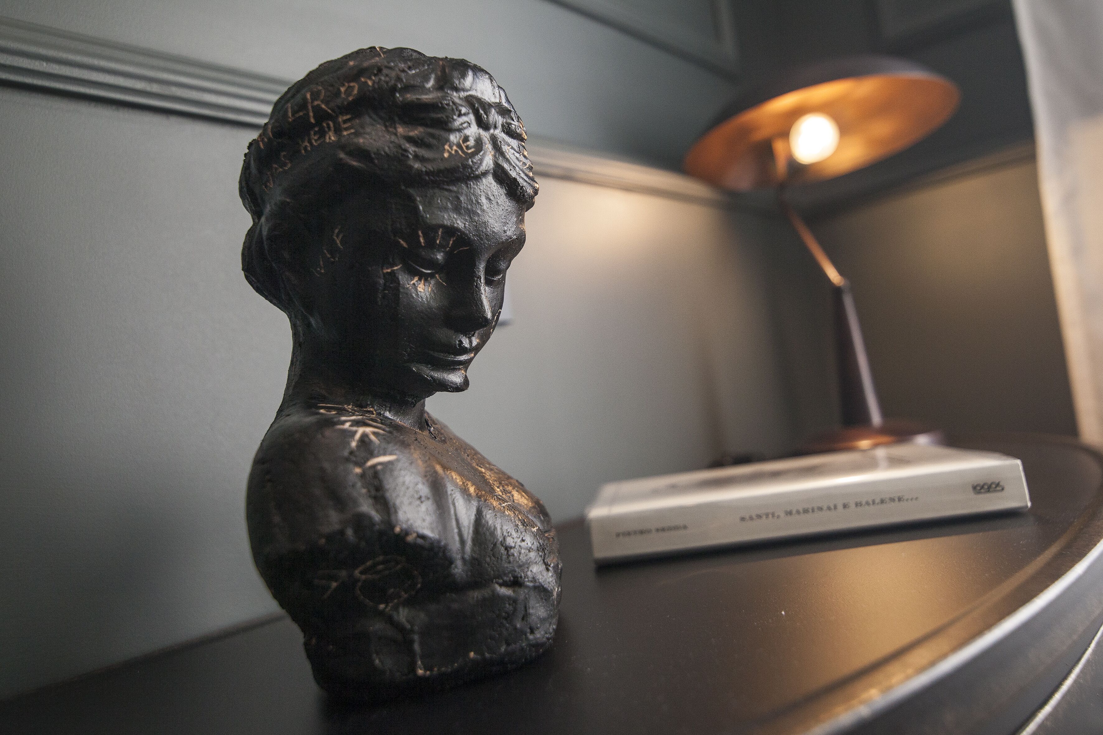 Une sculpture en buste est posée sur une table, à proximit é d’une lampe et d’un livre.