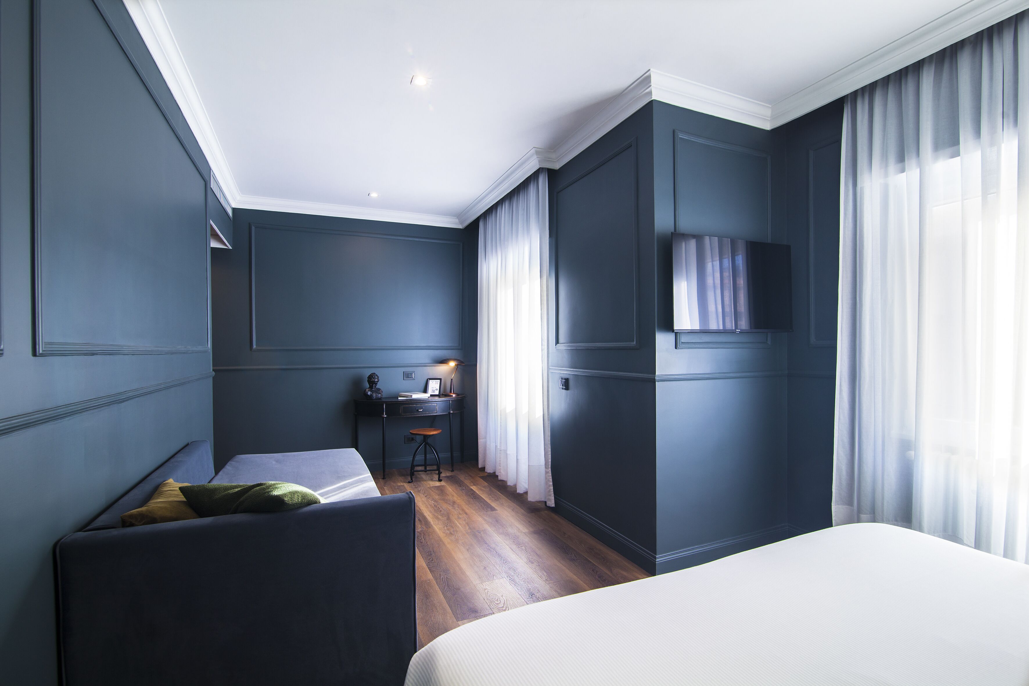 A modern hotel room with a large bed, a desk with a chair, and a television.