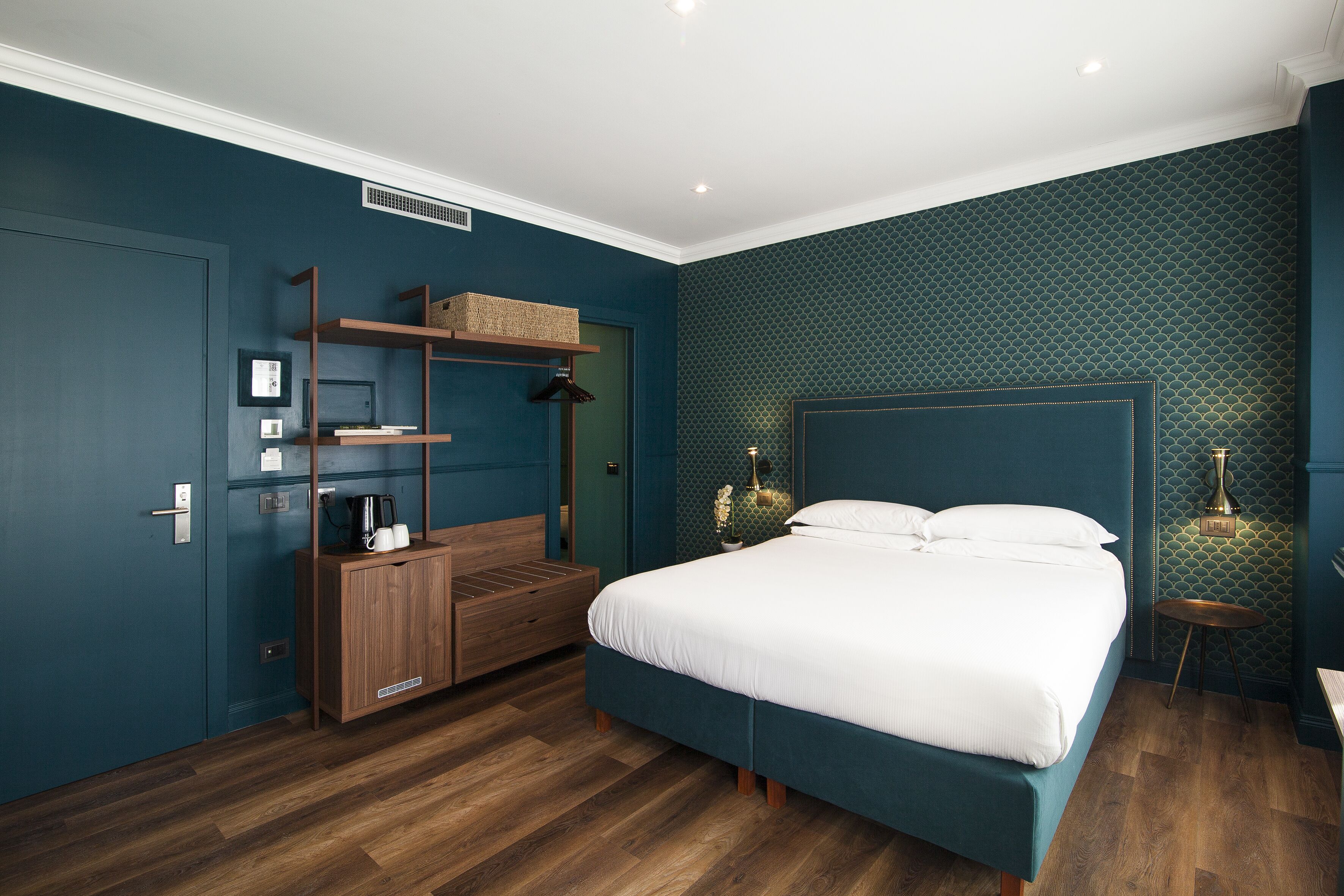 Een slaapkamer met een groot bed, een houten nachtkastje, een dressoir en een wandplank.
