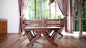 Una habitación con una mesa de madera y bancos, ventanas amplias con cortinas y vistas a zonas verdes.