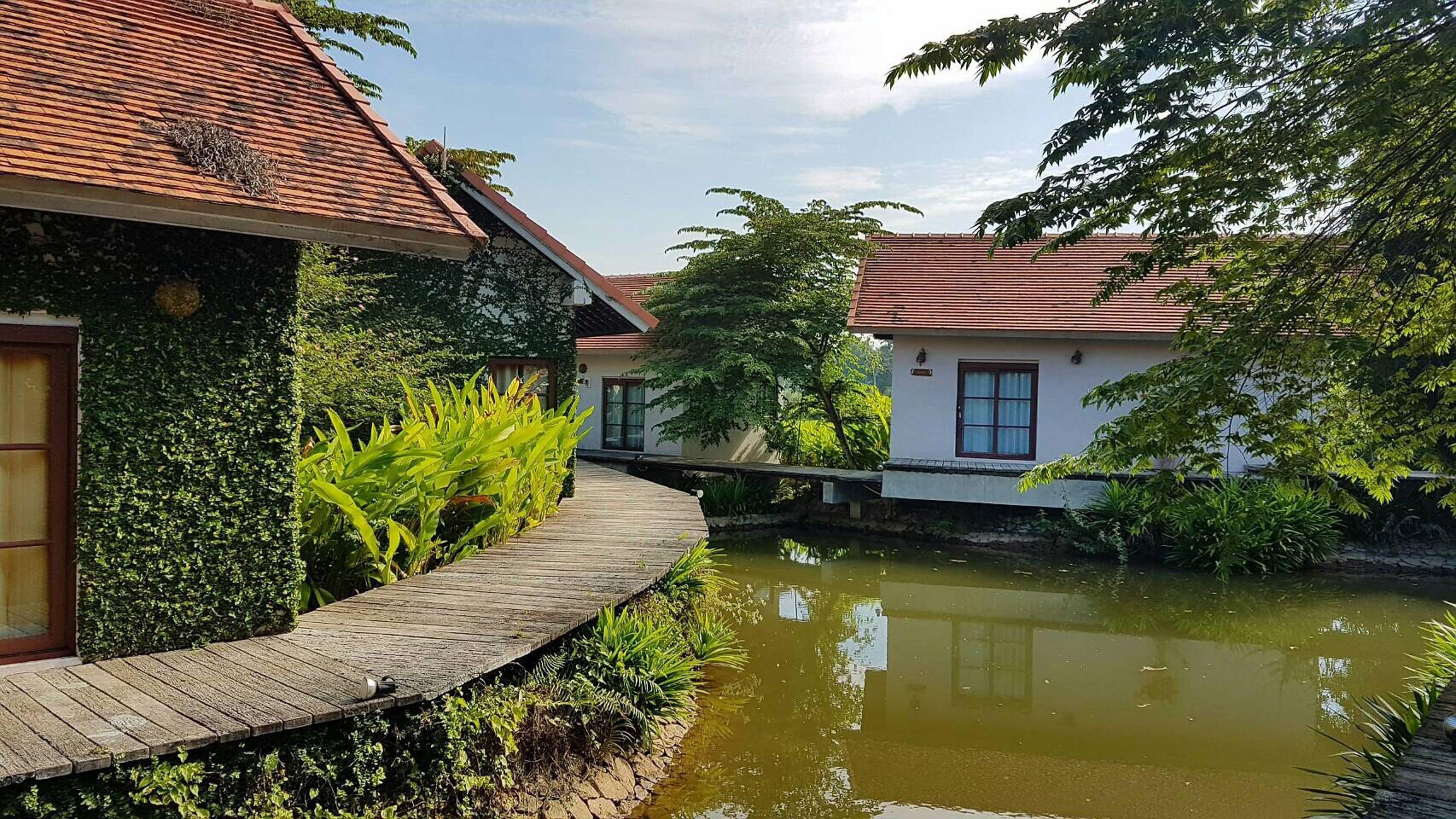 A traditional house with a tiled roof, a wooden pathway, and a calm water body.
