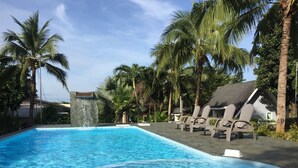 A swimming pool with lounge chairs, palm trees, and a waterfall feature. - A Little Villa (Krabi)