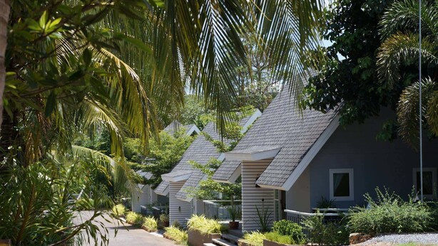 A row of small, single-story cottages with sloped roofs, surrounded by lush greenery and palm trees. - A Little Villa (Krabi)