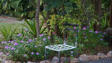 Uma cadeira de jardim de metal com encosto treliçado, rodeada por pedras e plantas floridas.