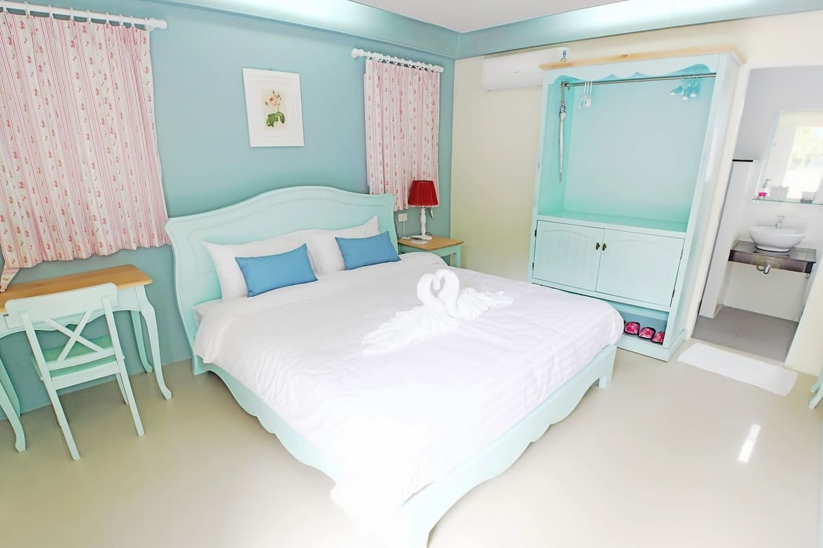 A bedroom with a bed, a desk, a chair, a vanity with a sink, and a shower area.