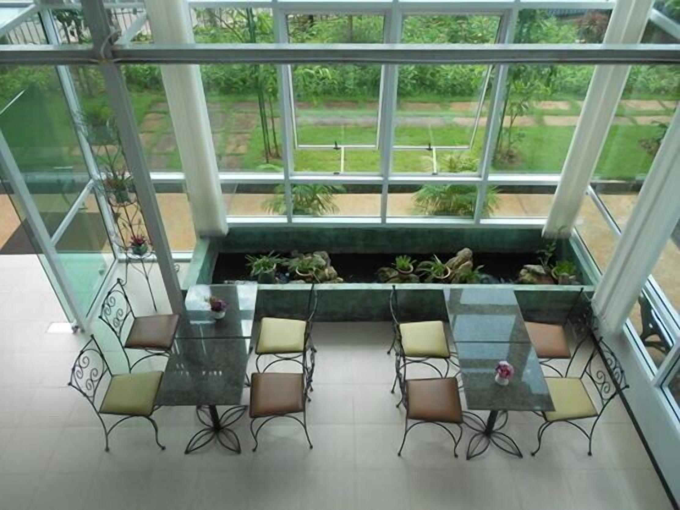 A conservatory with a glass ceiling, a dining table with chairs, and a view of a garden.