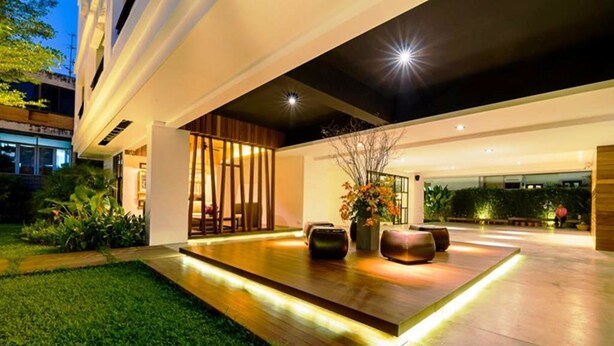 A modern outdoor patio with a wooden deck, seating area, and ambient lighting. - UMA Residence (Bangkok)