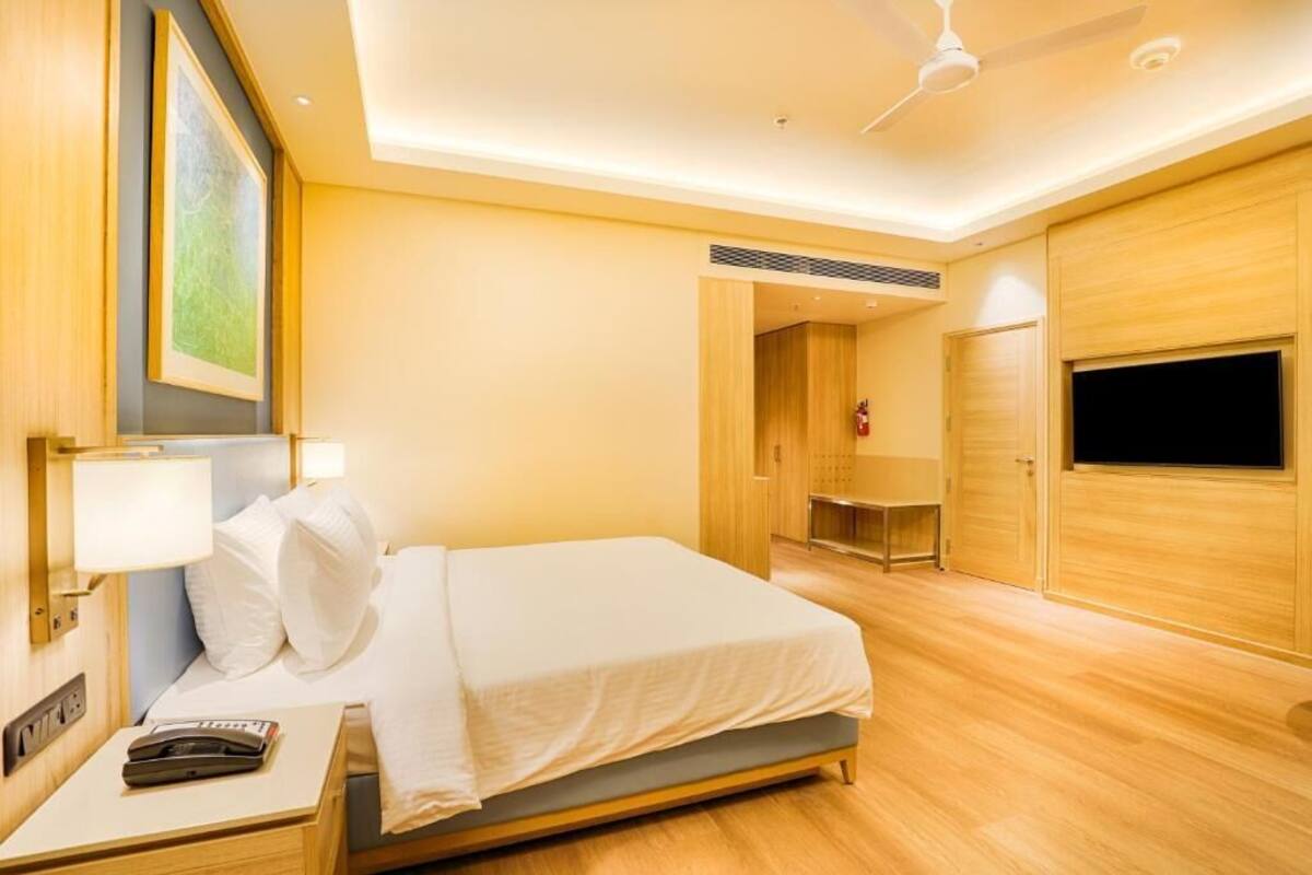 A hotel room with a bed, bedside table, lamp, ceiling fan, TV, and wooden walls.