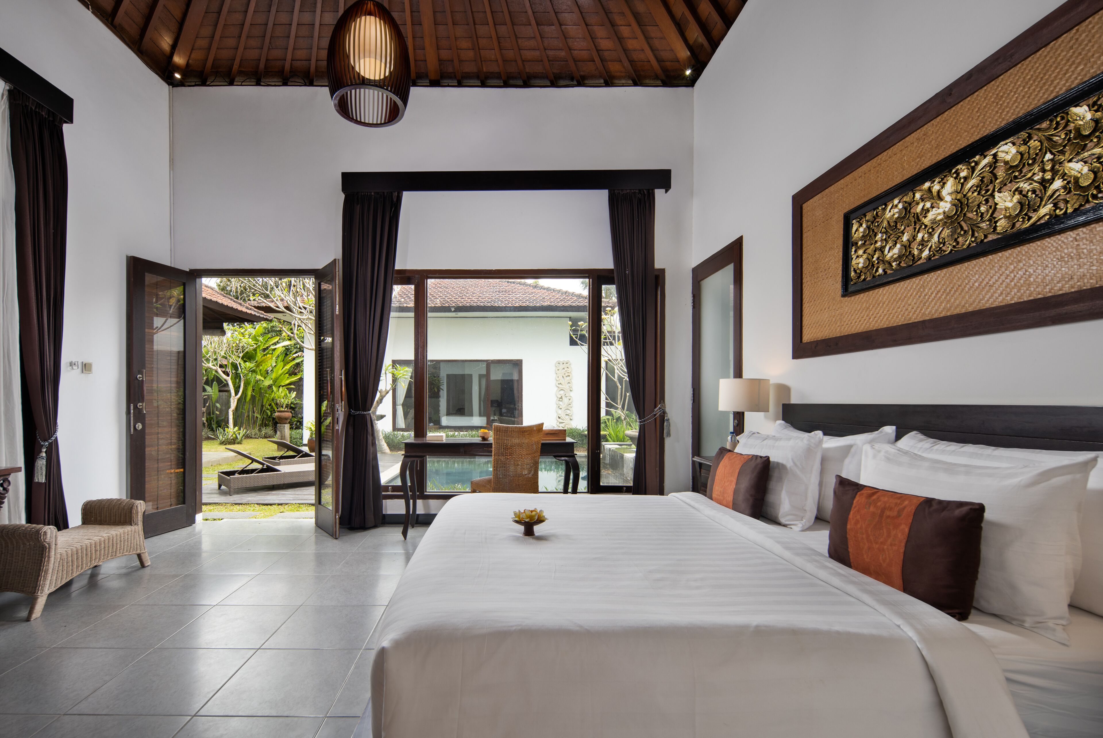 A hotel room with a large bed, a dining area with a table and chairs, and a view of a pool and greenery outside.