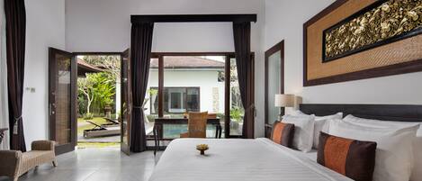 A hotel room with a large bed, a dining area with a table and chairs, and a view of a pool and greenery outside.