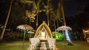 A nighttime outdoor wedding setup with a central aisle, white chairs, and umbrella canopies. - Ubud Raya Villa (Ubud)