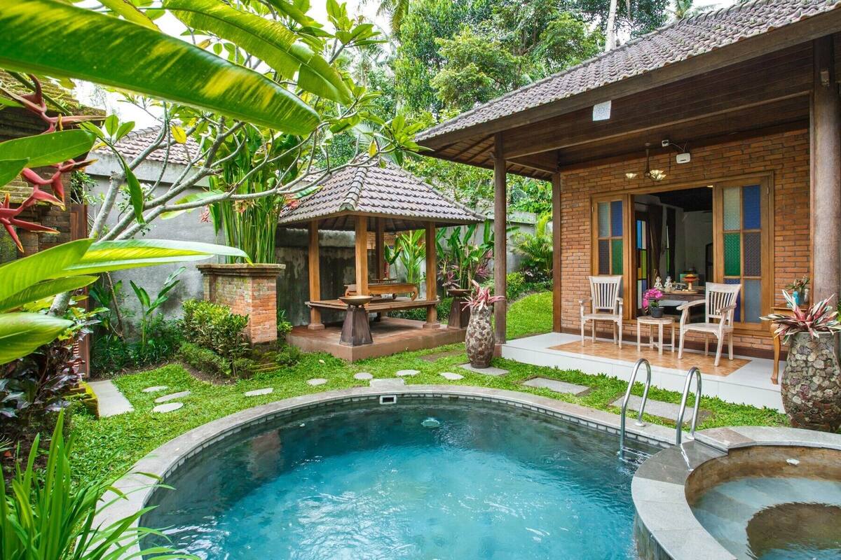 A pool area with a gazebo, a patio with chairs, and a brick building with glass doors.