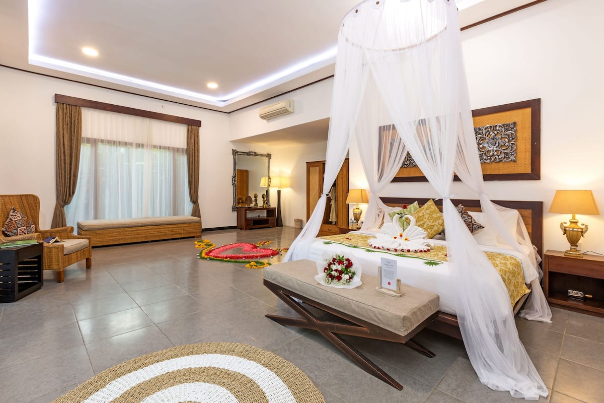 A hotel room with a canopy bed, a sofa, a bedside table, and a decorative rug.