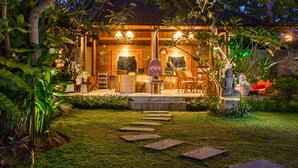 A well-lit outdoor area with a seating arrangement, a Buddha statue, and a pathway leading to a building with a tiled roof. - Ubud Raya Villa (Ubud)