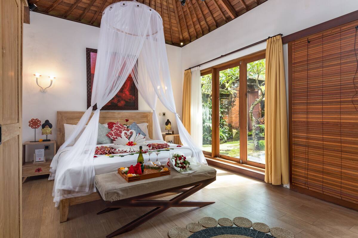 A bedroom with a canopy bed, bedside tables, a nightstand, and a view of the garden through a sliding door.