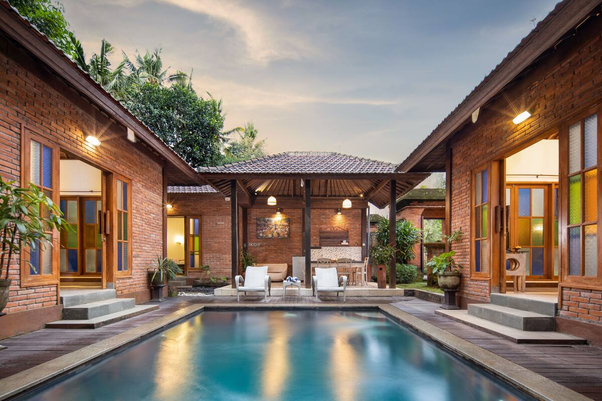 A pool area with two brick buildings, a covered patio, and seating.