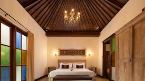 A bedroom with a wooden ceiling, a chandelier, a large bed with a wooden headboard, and a view through a window with colored glass panes. - Ubud Raya Villa (Ubud)