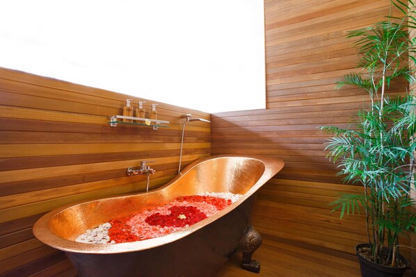 A bathtub with rose petals, wooden paneling, and a potted plant.