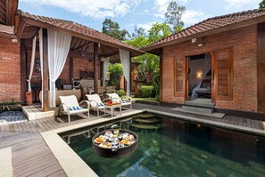 A poolside area with lounge chairs, a dining table with food, and a brick building with a covered patio.