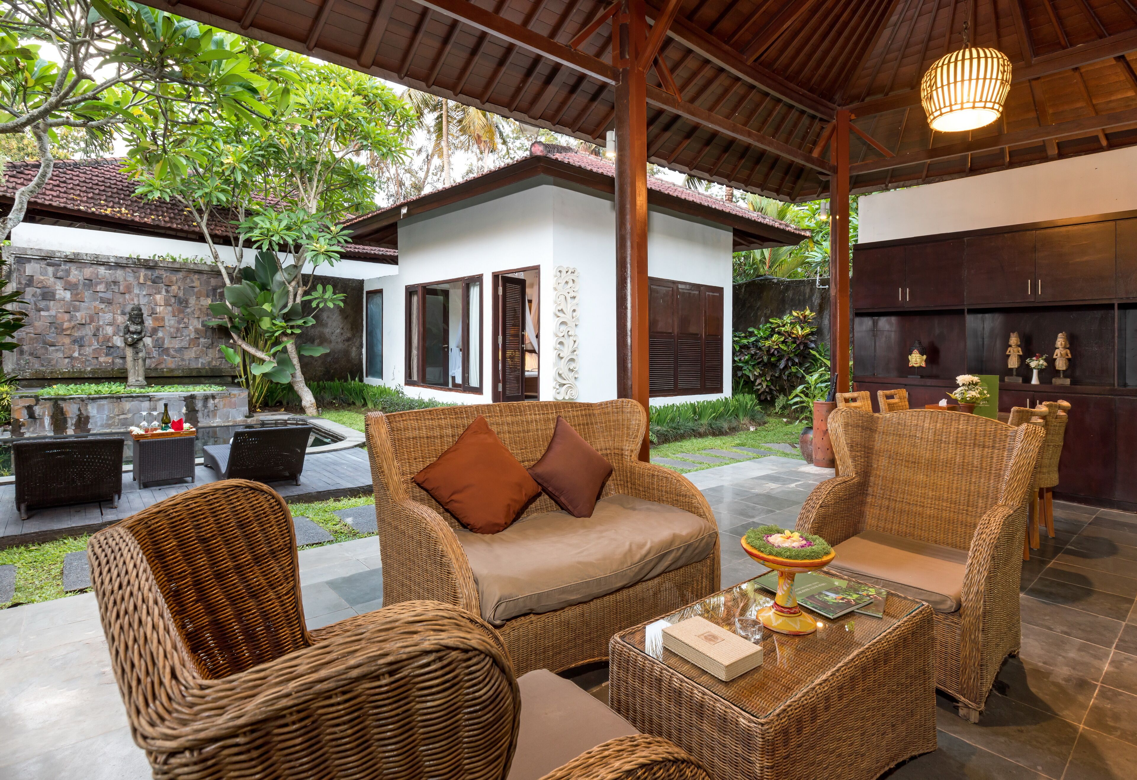 A wicker lounge area with a sofa and chairs, a small table with a decorative centerpiece, and a view of a house with a stone wall and a tiled roof.
