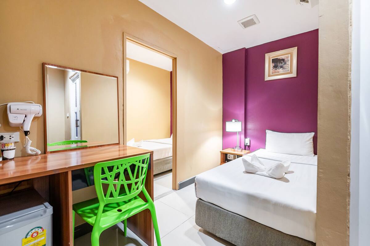 Une chambre d’hôtel comprenant un lit, un bureau avec une chaise, un miroir, un sèche-cheveux et une table de chevet avec une lampe.