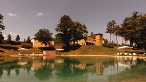 A swimming pool with lounge chairs and umbrellas, surrounded by trees and buildings. - Agriturismo San Galgano (Chiusdino)