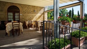 An outdoor patio with wooden tables and chairs, stone walls, and potted plants. - Agriturismo San Galgano (Chiusdino)