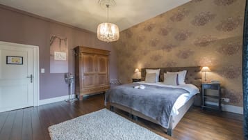 A bedroom with a large bed, a chandelier, a wooden wardrobe, and a patterned wallpaper.
