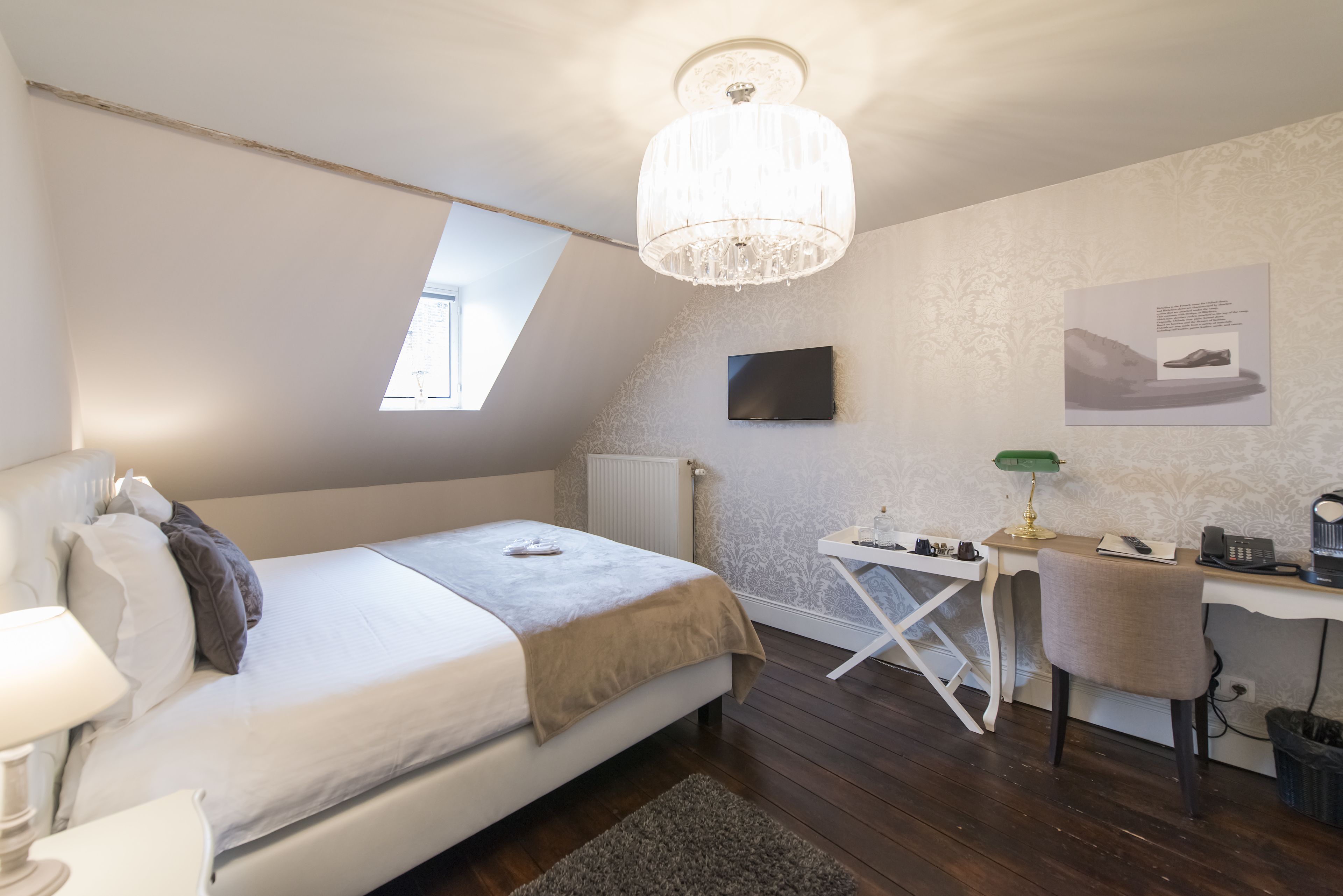 Een slaapkamer met een bed, bureau, stoel en een kroonluchter.