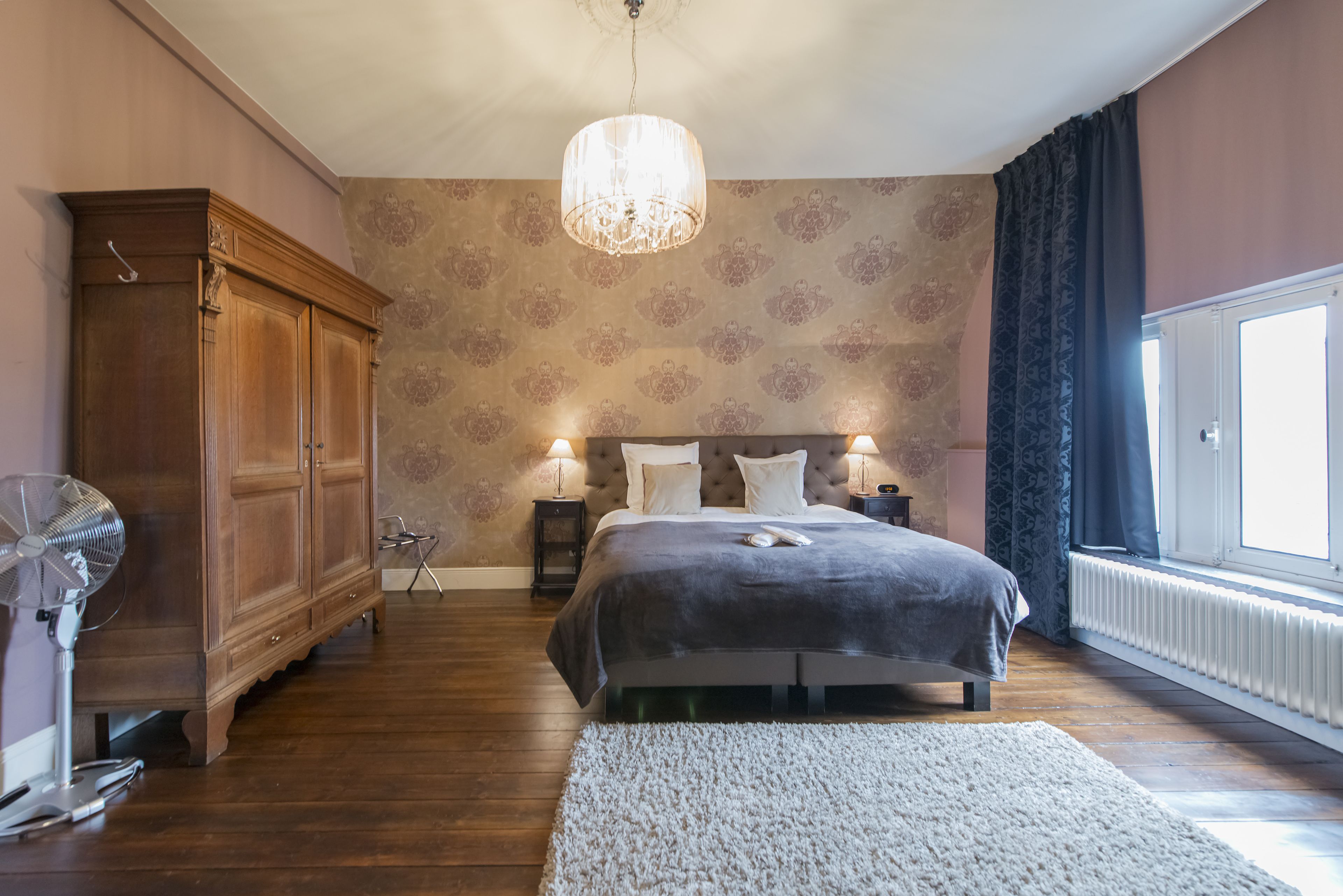 Un dormitorio con una cama grande, un armario de madera, un ventilador de pie y una araña.