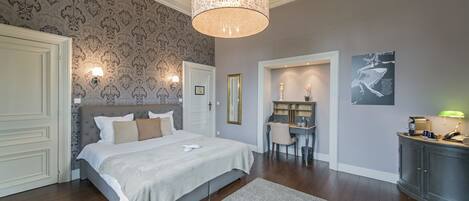 A bedroom with a large bed, a desk, and a chair, a wardrobe, and a wall with a patterned wallpaper and a framed picture.