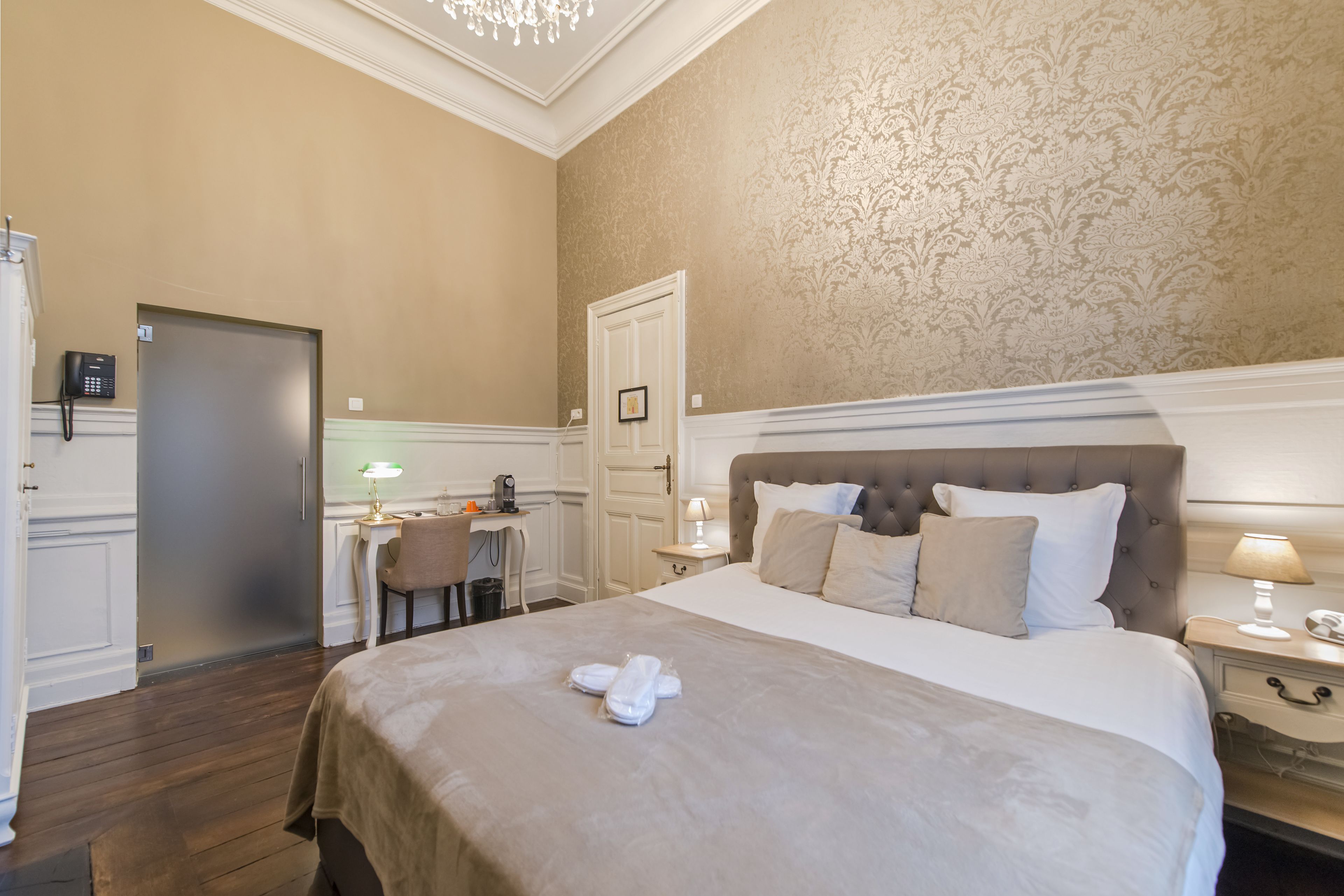 Une chambre d’hôtel avec un grand lit, un bureau, une chaise, un téléphone et une porte.