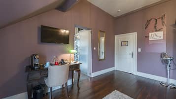 A room with a desk, chair, and a TV mounted on the wall. There is a door and a wall-mounted fan.
