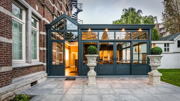 A modern conservatory with a glass roof, brick exterior, and two large urns in the foreground. - 't Huys van Steyns (Tongeren)