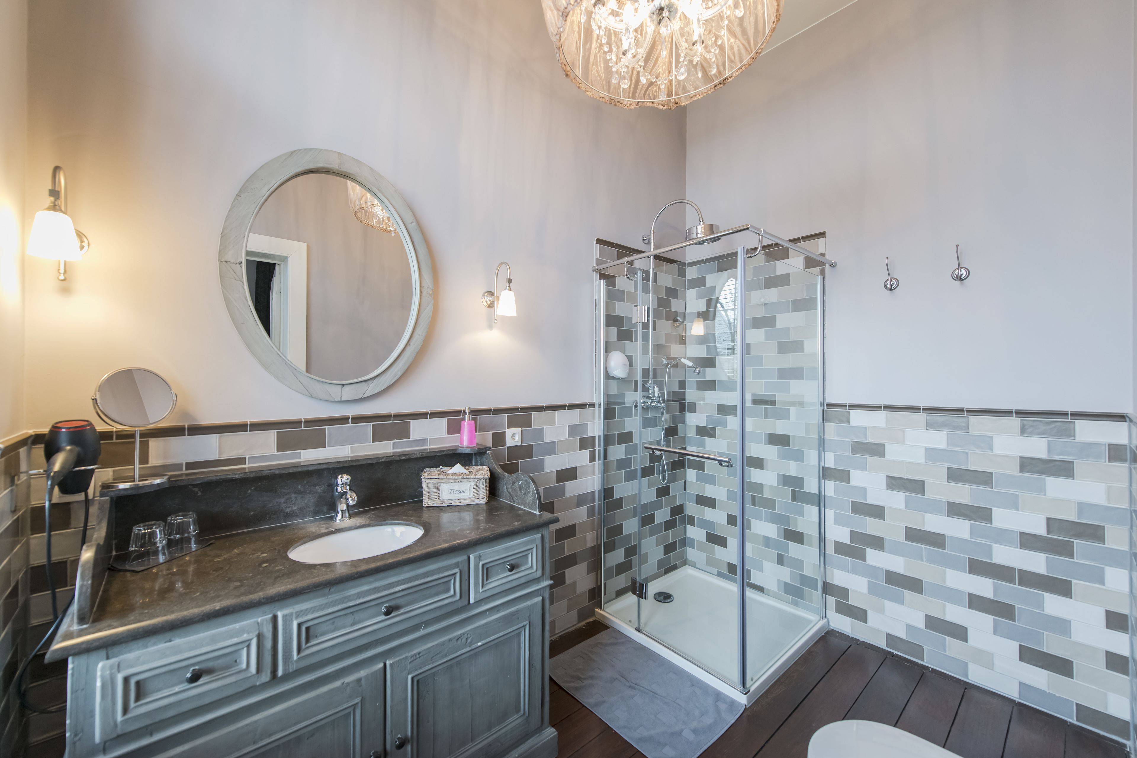 Un baño con ducha envuelta en vidrio, un espejo redondo y un lavabo con encimera oscura.