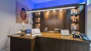 A reception desk with a wooden finish, a 'Reception' sign, a phone, a cash register, and a small plant.