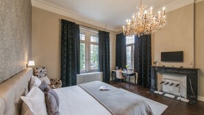 A hotel room with a large bed, a desk, a fireplace, and a television. - 't Huys van Steyns (Tongeren)