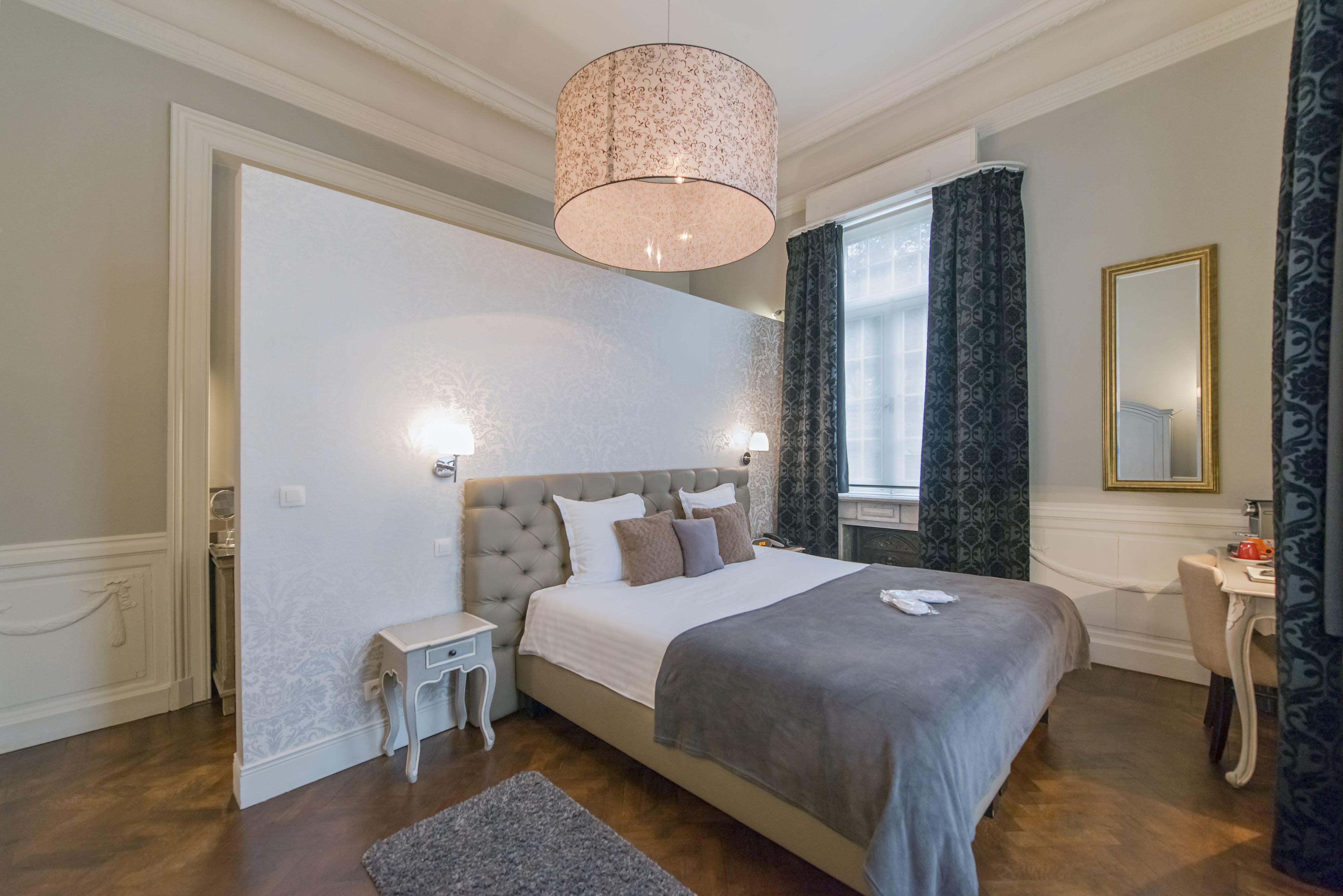 A bedroom with a large bed, bedside tables, a dresser, a mirror, and a window with curtains.