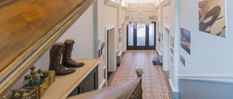 A grand hallway with a wooden staircase, a chandelier, and a patterned carpet.