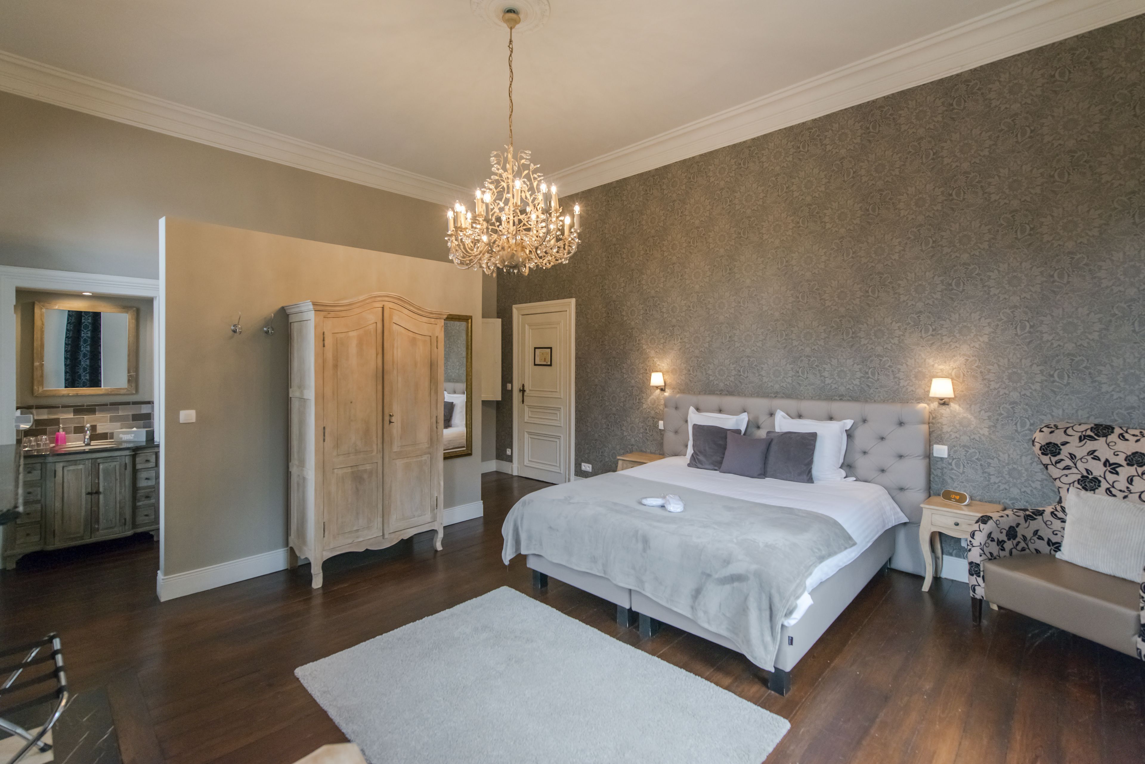 Een slaapkamer met een groot bed, een kroonluchter, een nachtkastje en een stoel.