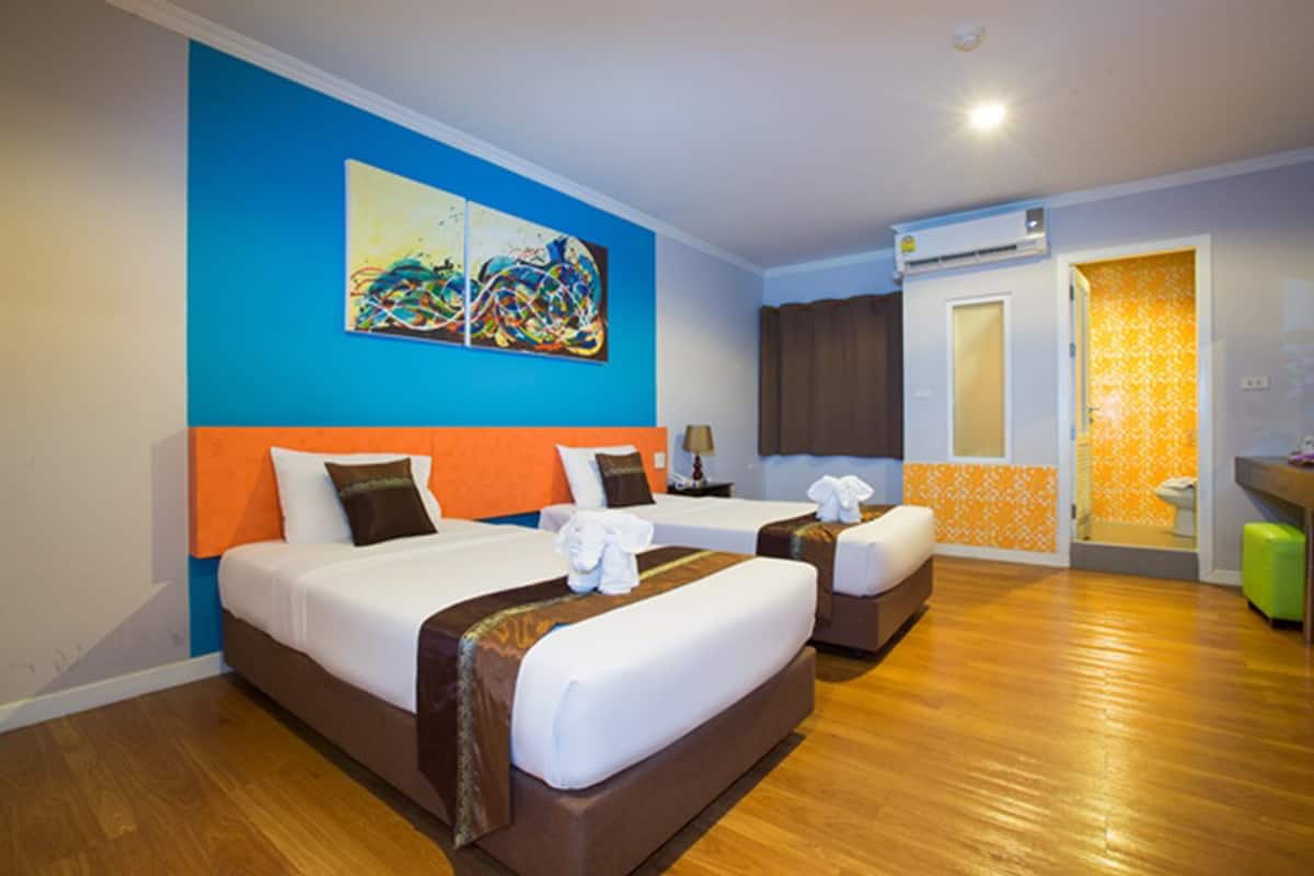 A hotel room with two beds, a large abstract painting on the wall, an air conditioning unit, and a bathroom visible through an open door.