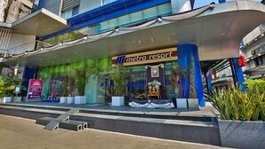 A modern hotel entrance with a Metro Resort sign, outdoor seating, and a landscaped area. - Metro Resort Pratunam (Bangkok)