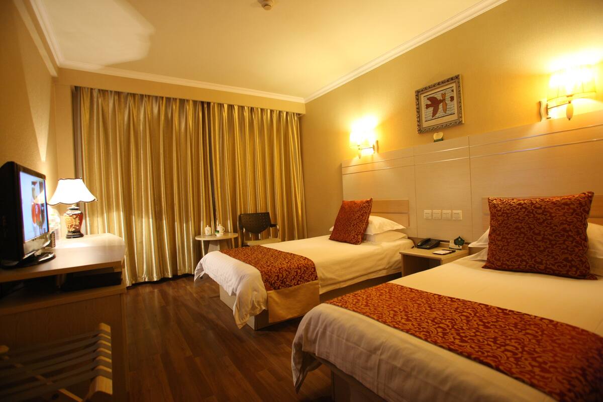 A hotel room with two beds, a television, a desk, and a chair.