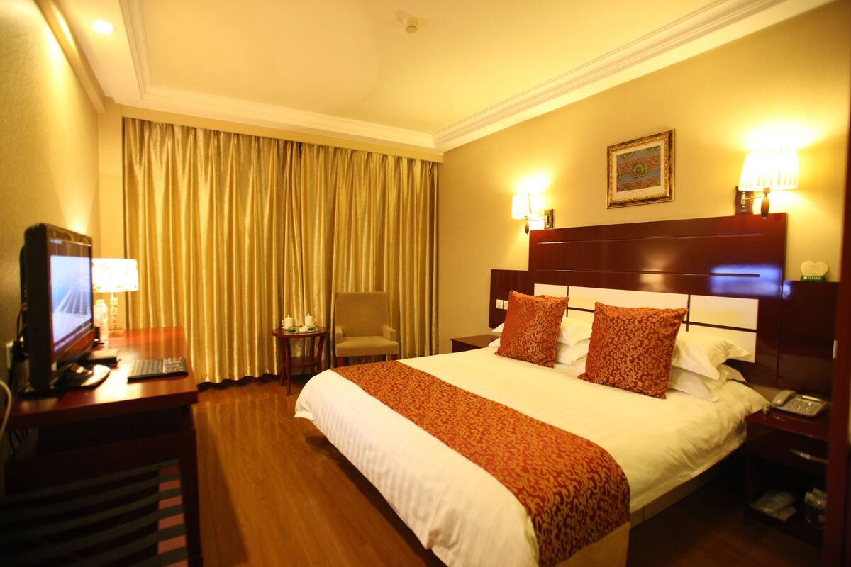 A hotel room with a large bed, a desk with a computer, a chair, and a lamp.