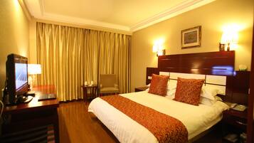 A hotel room with a large bed, a desk with a computer, a chair, and a lamp.