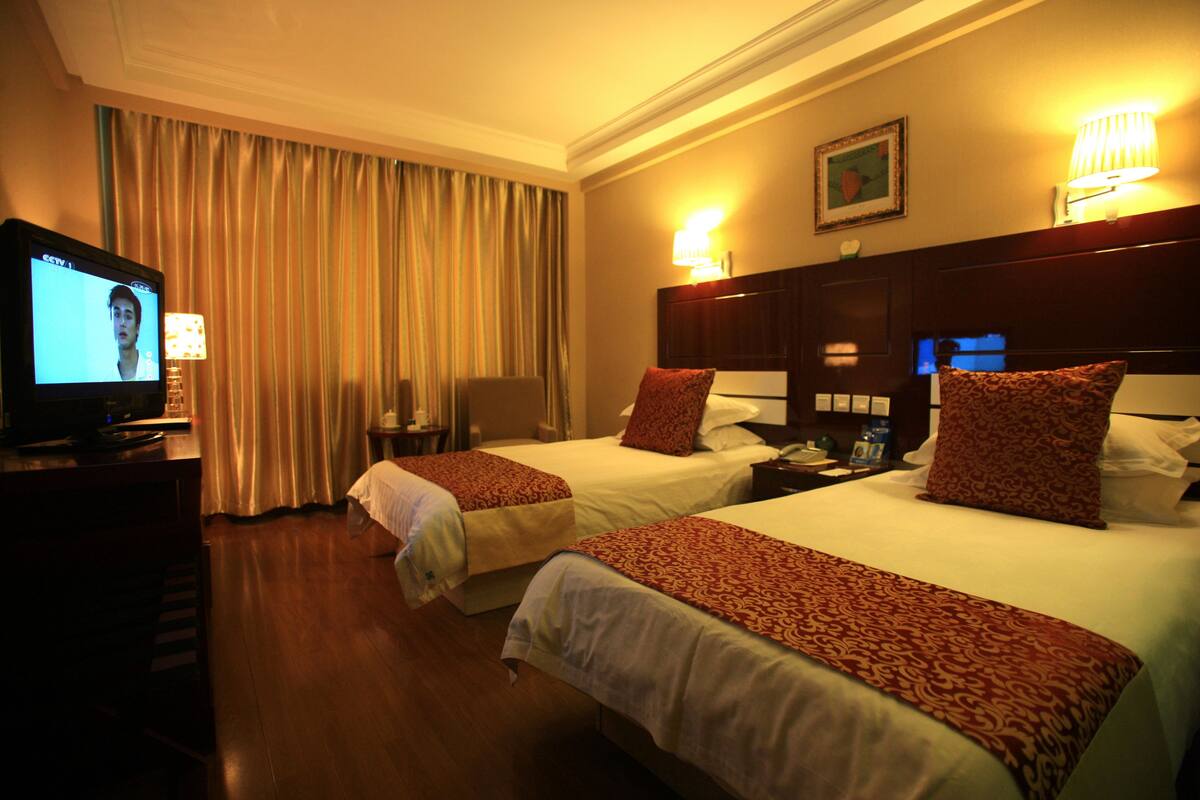 A hotel room with two beds, a TV, a desk, and a lamp.