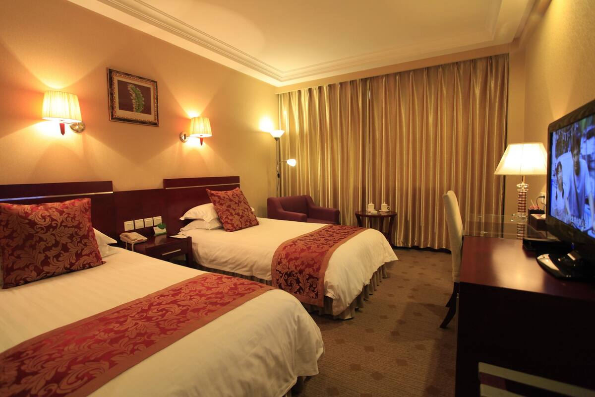 A hotel room with two beds, a television, and a desk.