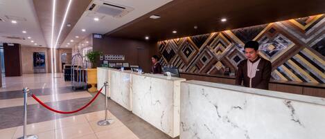 A hotel reception area with a marble counter, a red rope barrier, and a geometric patterned wall.