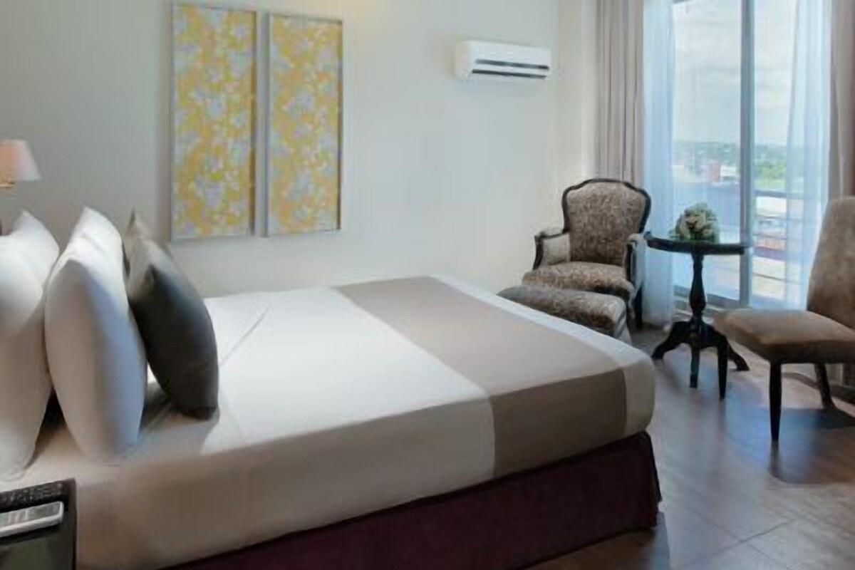 A hotel room with a bed, two chairs, a small table, and a large window.