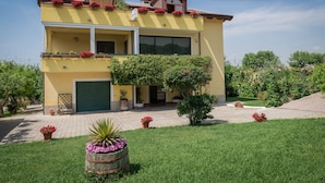 A two-story yellow building with a green garage door, a balcony with red flowers, and a well-maintained lawn. - B&B Il Girasole (Agropoli)